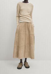 Pull en maille beige et longue jupe en daim fauve avec poches latérales, présentant une texture lisse et une taille élastique, assortis à des sandales fauves.