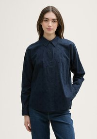 Navy blue shirt made of cotton, featuring a textured pattern of small raised dots, long sleeves, and a classic collar. Button-up front design.