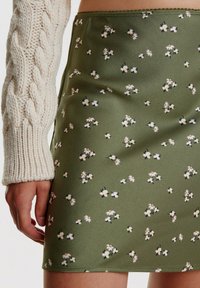 Groene bloemen mini-jurk met kleine witte en gele bloemen op een gladde, textuurstof; gecombineerd met een gebreide crèmekleurige trui.