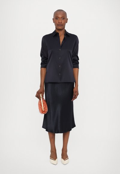 Navy satin shirt with long sleeves and button-up front; matching satin midi skirt; coral handbag; pointed beige heels.