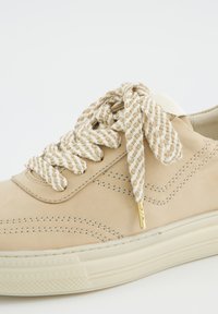 Baskets beiges en cuir lisse, lacets crème texturés avec un motif, coutures minimales et semelle en caoutchouc plate.