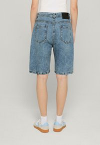 Hellblaue Denim-Shorts mit lockerer Passform, fünf Taschen und fransigem Saum. Die Rückseite hat zwei aufgesetzte Taschen und ein schwarzes Taillenlabel.