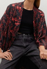 Kimono noir à motif floral rouge, tissu léger, coupe ample, manches larges, porté avec un haut noir ajusté et un jean denim foncé.