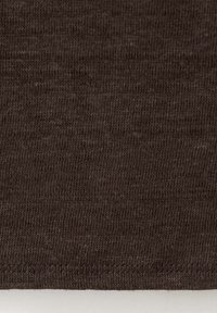 Gros plan d'un tissu tricoté brun foncé avec une couture horizontale visible près du bord inférieur sur un fond clair.