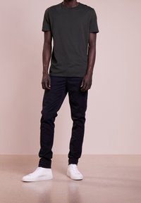 T-shirt verde scuro a maniche corte, abbinato a pantaloni tapered blu navy e sneakers bianche. Design semplice, materiale in cotone e colletto a girocollo.
