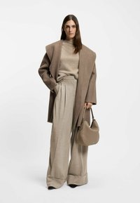 Oversized brown wool coat over a beige sweater, paired with wide-leg beige trousers and a taupe leather handbag. Smooth textures and muted colors.