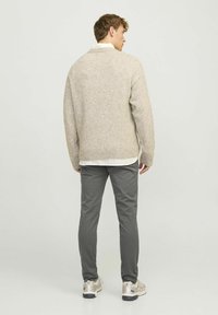 Suéter de punto beige con cuello redondo, usado sobre una camisa blanca con cuello, combinado con pantalones grises y zapatillas, visto desde la parte de atrás.