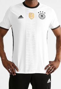 Vit fotbollströja med svarta accenter, rund hals, med Tysklands logotyp, FIFA-märke och fyra stjärnor. Tillverkad av lättviktig tyg.