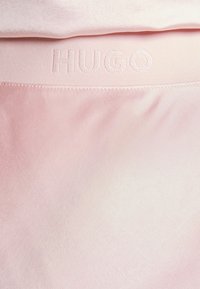 Vaaleanpunainen kangas, jossa on sileä pinta; siinä on hillitty "HUGO" -logo nostetussa brodeerauksessa joustovyön varrella.