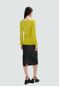 Maglione lavorato a maglia verde chiaro con maniche lunghe, abbinato a una gonna midi in ecopelle nera con spacco posteriore e sandali con tacco.
