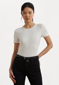 Vit t-shirt med kort ärm som har rundad halsringning, mjuk textur och figurnära design, kombinerad med hög midja svarta jeans och ett bälte.