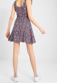 Vestido skater con estampado floral en morado, rosa y negro, con un corsé ajustado, falda acampanada y escote redondeado. Combinado con zapatillas blancas.