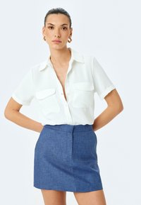 Witte korte mouwen shirt met twee borstzakken en een kraag, gecombineerd met een blauwe getextureerde minirok met een rechte snit en een achternaad.