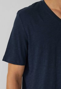 Granatowa koszulka z krótkim rękawem, wykonana z lekkiego materiału. Posiada dekolt w serek oraz subtelną fakturę, z czystym wykończeniem brzegu.