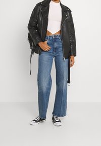 Chaqueta de motorista de cuero negro con flecos, top corto de rayas blancas ajustado, jeans de tiro alto en azul claro y zapatillas negras.