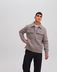 Hall ja zip-up jakk, mis on valmistatud tekstuuriga kangast ja millel on kaks esimest taskut. Kombineeritud heleda sviitriga all ja sobitatud tumedate pükstega.