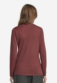 Långärmad topp i en djup rostfärg, tillverkad av mjukt material, med en enkel rund halsringning och en avslappnad passform.