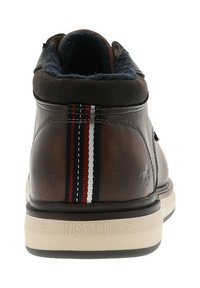 Chaussure montante en cuir marron avec un col rembourré bleu marine, un accent rayé rouge, blanc et bleu, et une semelle en caoutchouc blanche portant la marque "MUSTANG".