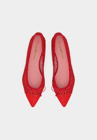 Ζευγάρι κόκκινα μπαλαρίνια με μυτερή μύτη, με γεωμετρικά σχέδια που έχουν κοπεί με λέιζερ και μικρά διακοσμητικά φιογκάκια στην κορυφή, σε λευκό φόντο.