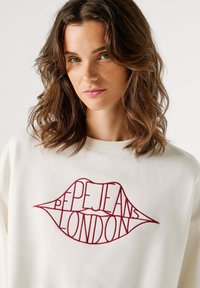 Sudadera blanca con un diseño de labios bordados en rojo que incluye el texto "PEPE JEANS LONDON" integrado en la forma de los labios.