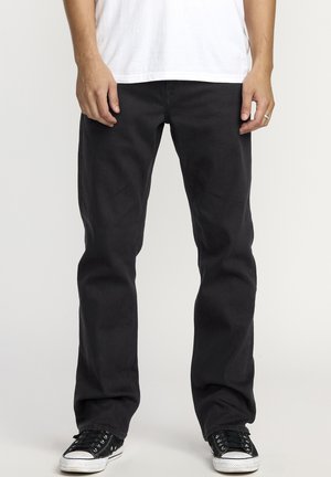 Black cotton jeans with a relaxed fit, featuring five-pocket design, belt loops, and subtle stitching, paired with black low-top sneakers.