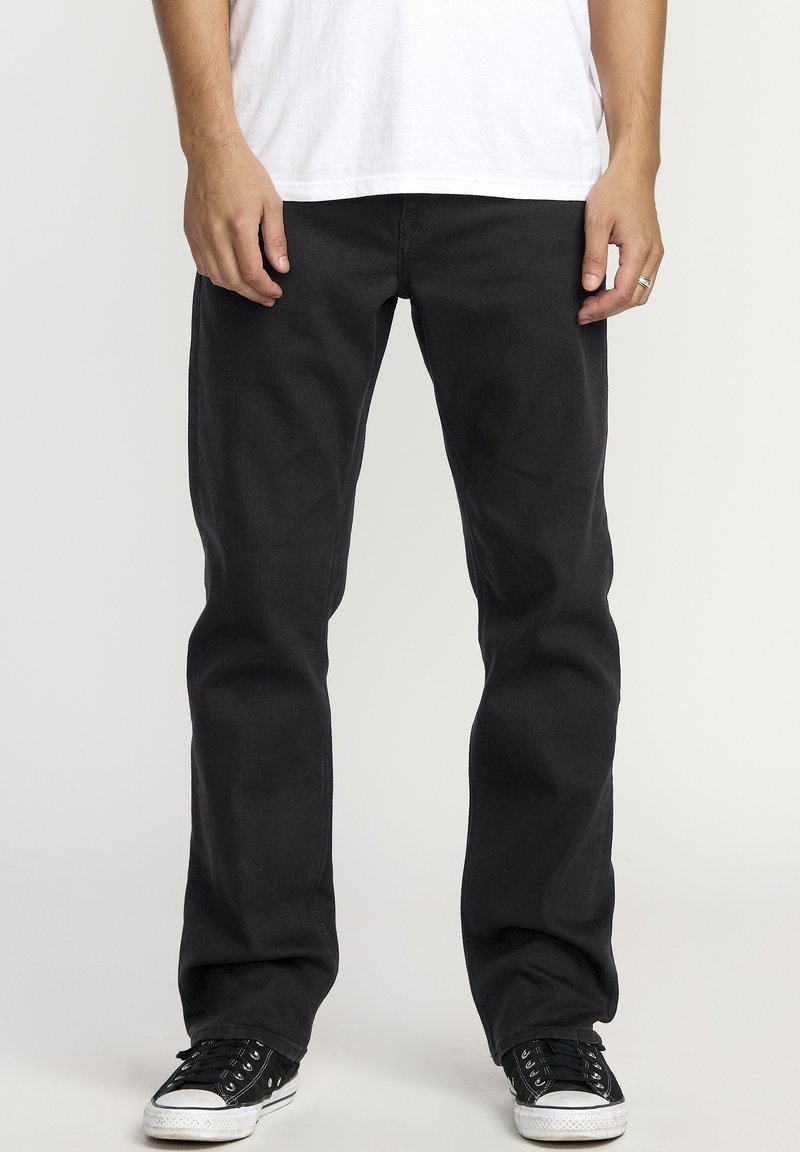 Jean noir en coton avec une coupe décontractée, dotés d'un design à cinq poches, de passants de ceinture et de coutures discrètes, associés à des baskets basses noires.