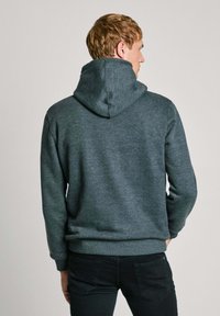 Felpa grigia scura con cappuccio regolabile, polsini e orlo a coste. Il tessuto sembra morbido e strutturato, con una vestibilità casual.