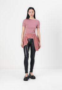 Rosa tettsittende kortermet topp, svarte høytlivleggings, rød rutete skjorte knyttet i livet, og svarte chunky sko. Enkelt design, glatte teksturer.