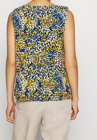 Haut sans manches à motif floral en noir, jaune, bleu et blanc, avec une coupe décontractée et des accents aux épaules. Texture de tissu douce.