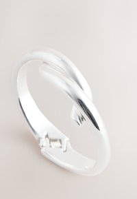 Silver metal bracelet featuring a smooth, twisted design with a glossy finish and a secure clasp detail.