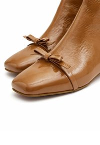 Zapatos de charol marrón con punta cuadrada, que presentan un lazo decorativo en la parte delantera y un acabado suave y brillante.