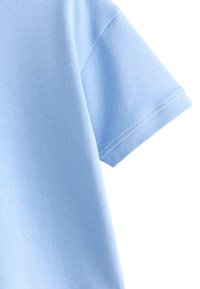 Svijetloplava pamučna majica s okruglim izrezom i kratkim rukavima s rebrastim rubovima, prikazuje glatku teksturu i čiste linije.