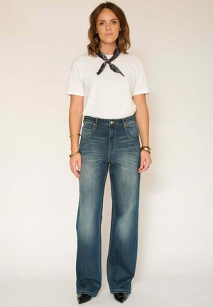 Jean en denim bleu clair à jambes larges avec une taille haute, doté de poches avant et d'un léger délavage ; accompagné d'un t-shirt blanc uni et d'une écharpe noire.