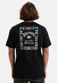 Black cotton t-shirt with colorful geometric print featuring the "Billabong" logo and text. Relaxed fit, short sleeves, and minimal design.