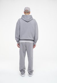 Felpa grigia con cappuccio e coulisse, abbinata a pantaloni della tuta grigi coordinati. Design semplice; texture liscia. Include un berretto grigio.