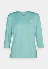 Helltürkises Shirt mit drei Viertelärmel, einem V-Ausschnitt und kleinem Logo auf der Brust; mit korallenfarbenen Akzenten an den Ärmelenden.