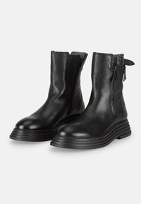 Stivaletti in pelle nera con finitura testurizzata, cerniere laterali e suole in gomma nera robusta con design impilato.