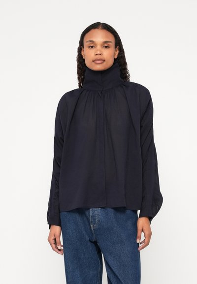 Blouse longue à manches en marine avec col haut, devant plissé et coupe décontractée. Fabriquée en tissu léger au toucher doux.