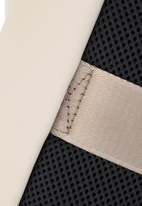 Mřížkovaná tkanina v černé barvě s béžovým popruhem. Popruh má viditelné prošívání a šikmý designový prvek, který přidává strukturu a detaily.