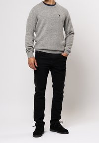 Grå ulltröja med rund hals, prydd med en liten logotyp. Matchas med svarta slim-fit byxor och svarta mockaskor.