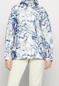 Chaqueta impermeable blanca con patrón abstracto azul, que presenta un cuello alto, capucha ajustable y cierre frontal con cremallera. Textura suave.