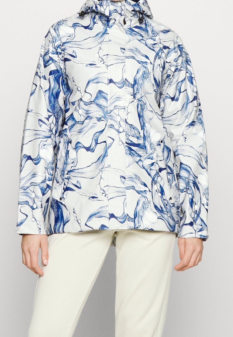 Chaqueta impermeable blanca con patrón abstracto azul, que presenta un cuello alto, capucha ajustable y cierre frontal con cremallera. Textura suave.