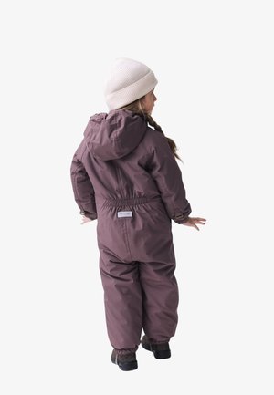 Lila wasserdichter SchneOverall mit Kapuze, elastischem Bund und Reißverschlussärmeln, kombiniert mit einer beigen, gerippten Strickmütze und schwarzen Stiefeln.