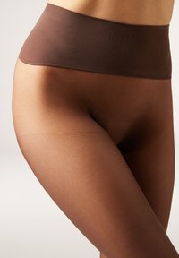 Medias transparentes marrones con una cinturilla ancha y lisa. Presentan una textura acanalada en las piernas, creando un patrón sutil en toda su extensión.