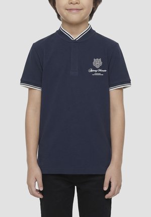 Kind draagt een navyblauw poloshirt met korte mouwen, een witte gestreepte kraag en mouwen, en een klein geborduurd logo op de borst.