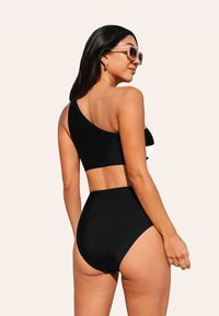 Zwarte bikini set met een top met één schouder en hoge taillebroekjes. Gladde stoftextuur met minimale kleurcontrasten in het ontwerp.