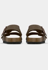 Pruunid sandaalid, millel on kaks laia rihma, kinnitused ja pehme korkaluspadi. Must kummist välispind ja avatud varba disain nähtav tagant.