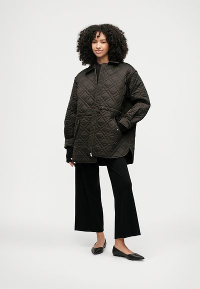 Καπιτονέ μαύρο μπουφάν εξωτερικής ένδυσης με γιακά, μπροστινές τσέπες και ρυθμιζόμενο κορδόνι. Συνδυασμένο με μαύρα παντελόνια φαρδιάς γραμμής και επίπεδα παπούτσια.