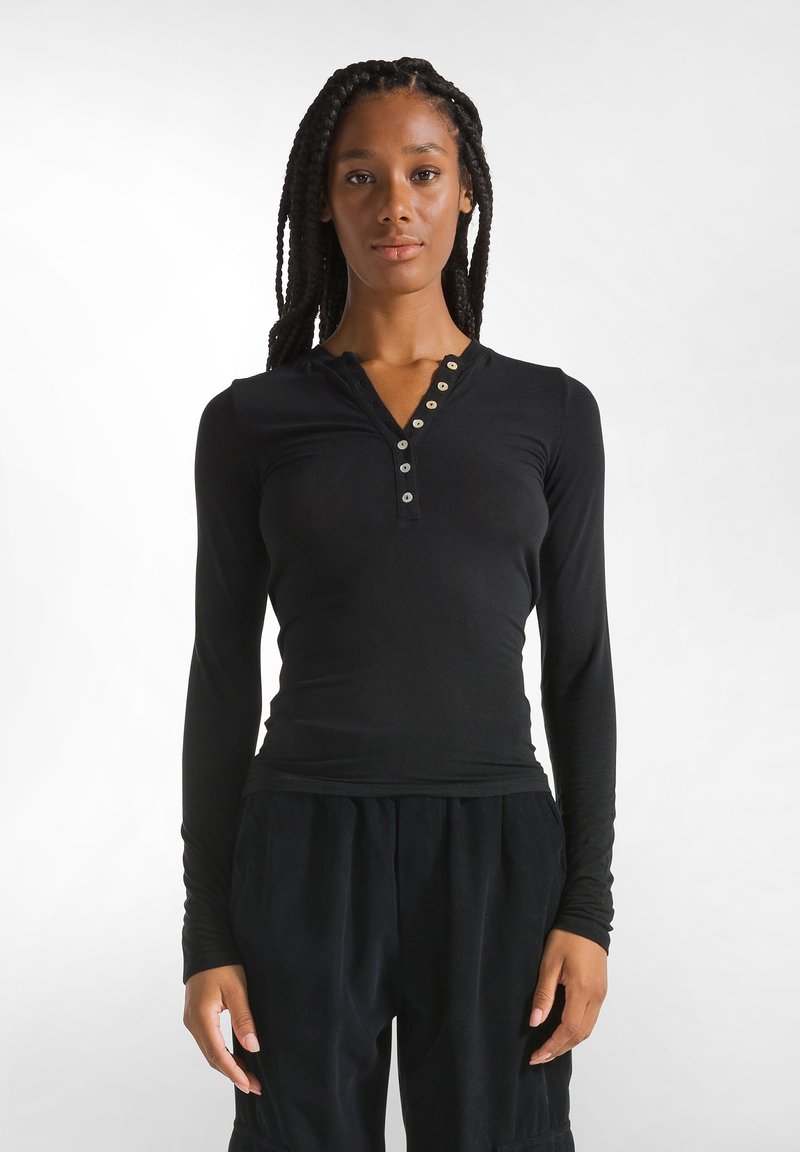 Schwarzes Langarmshirt mit Henley-Ausschnitt, das eine Reihe von fünf metallischen Knöpfen vorne hat. Weicher, figurschmeichelnder Stoff.