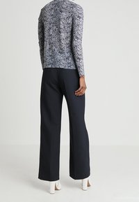 Langärmeliges Oberteil mit Schlangenmotiv in Schwarz und Weiß; kombiniert mit weit geschnittenen schwarzen Hosen; Model trägt weiße Absatzstiefel.